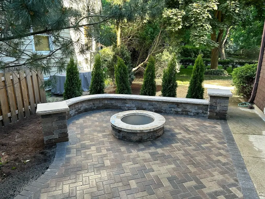 Round fire pit on a paver patio with a stone seat wall