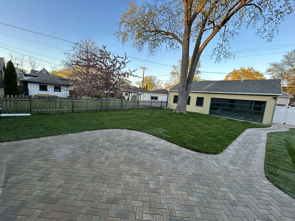 Newly installed sod lawn in a backyard next to a paver driveway