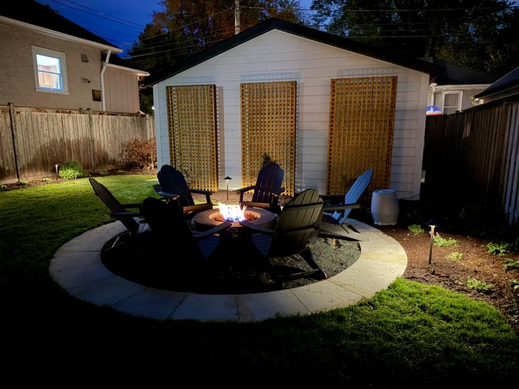 Fire pit and Adirondack chairs on a round patio lit up at night